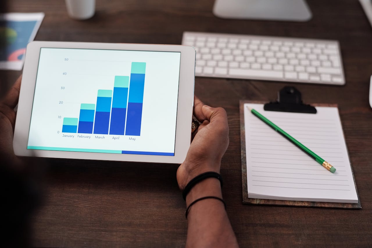 about-02 Close-up of a person holding a tablet showing growth charts on a wooden desk setup.